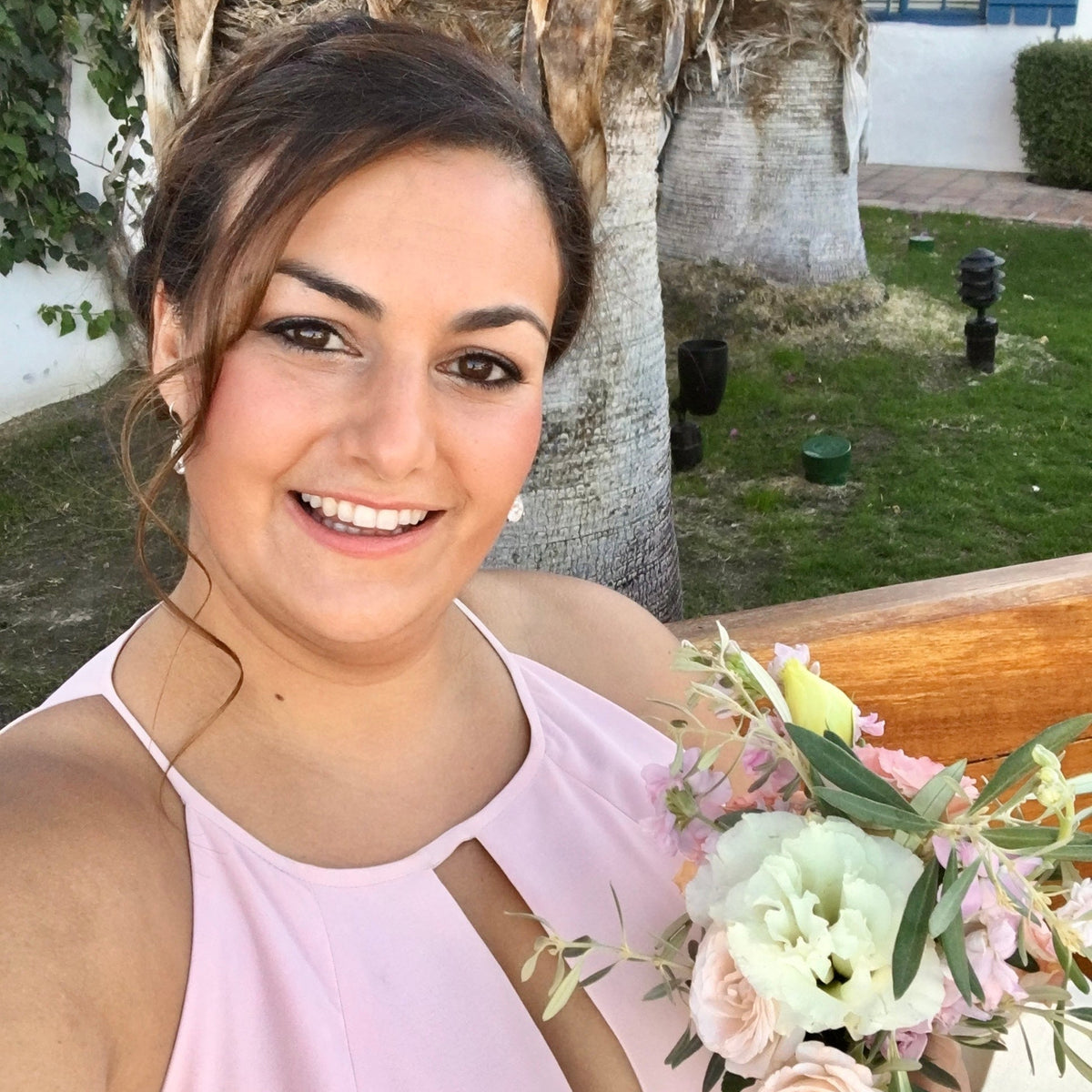 Woman holding a bouquet of flowers in an outdoor setting with trees and a building in the background.